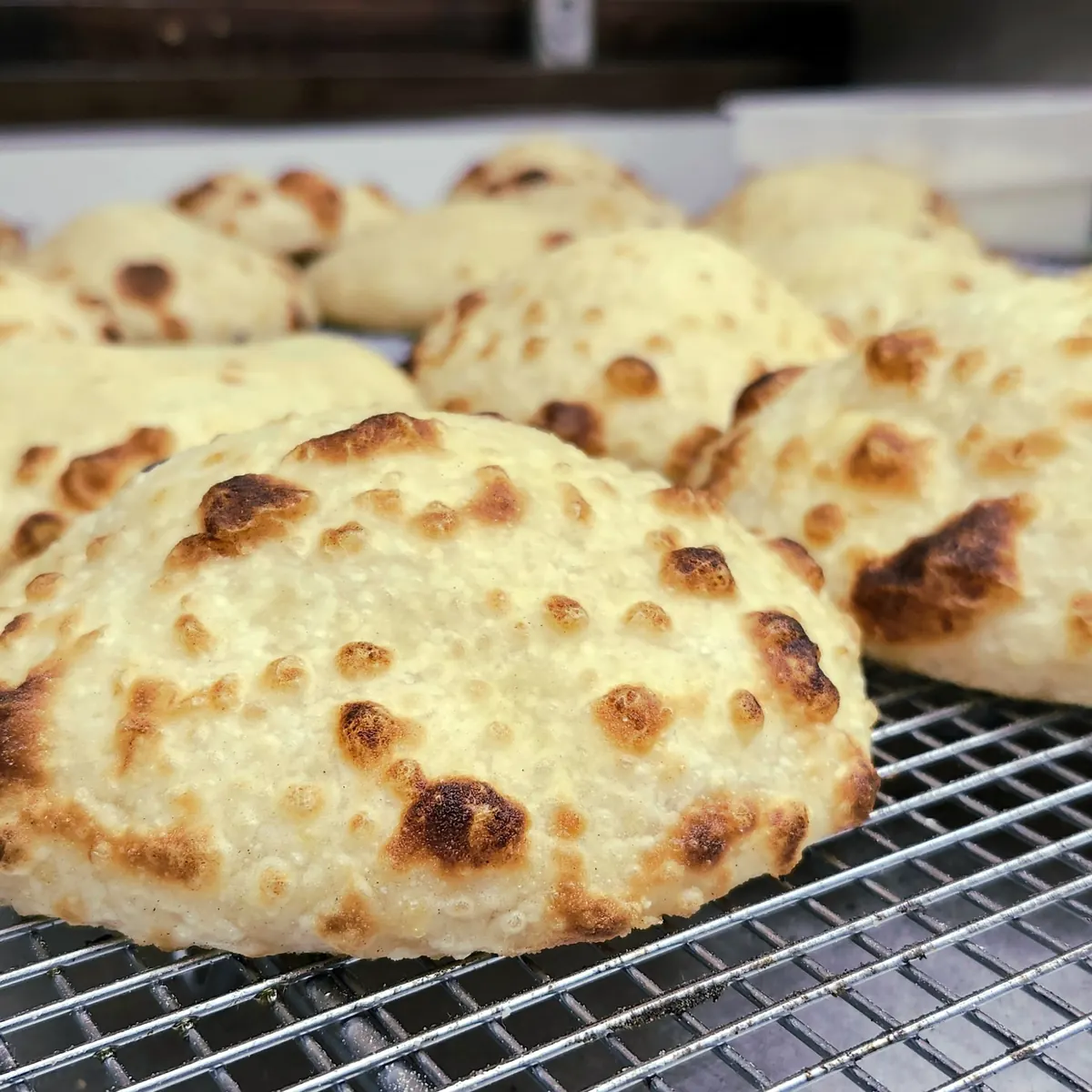 Freshly baked round breads with charred spots cooling on a wire rack