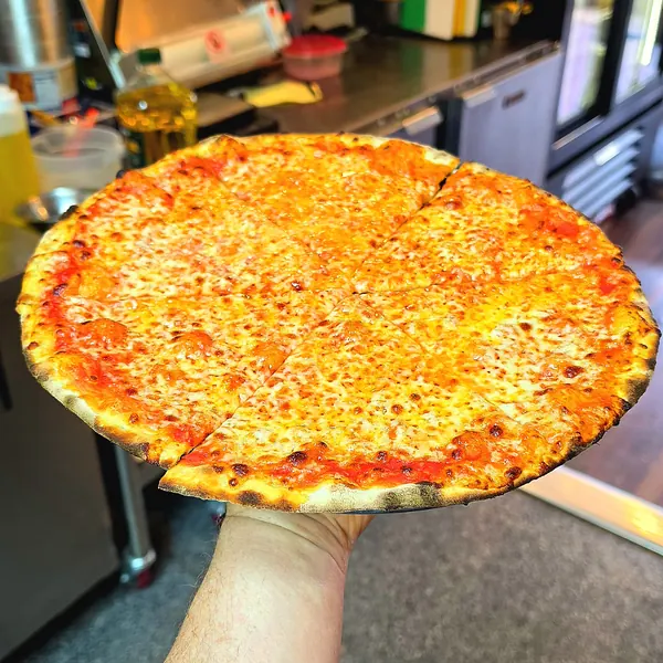 A hand holding a sliced thin-crust cheese pizza in the kitchen