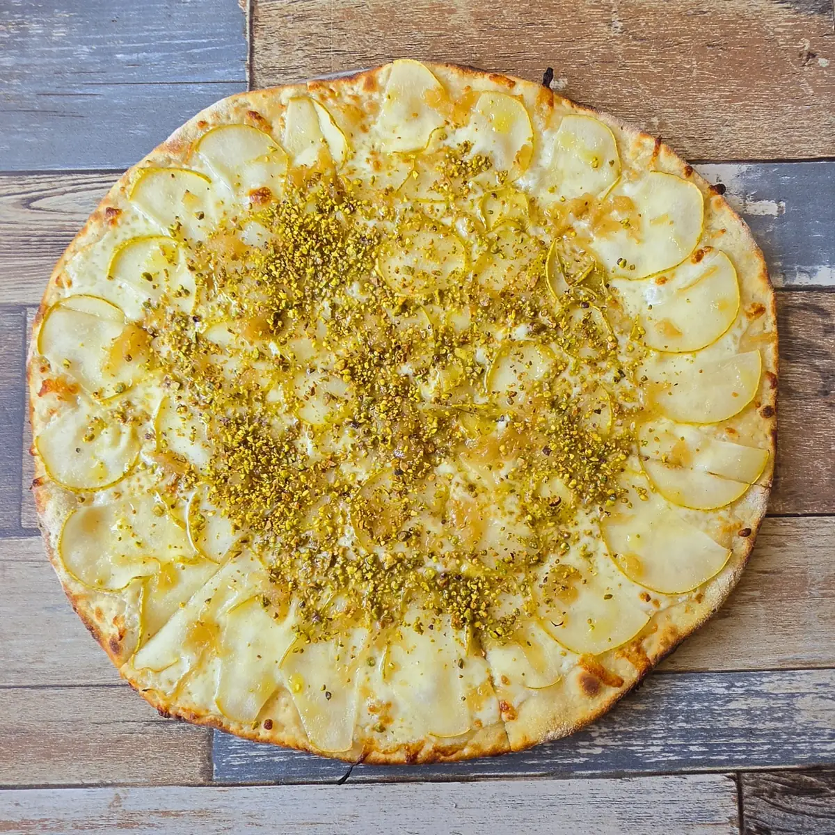 A white pizza covered in thin pear slices and crushed pistachios