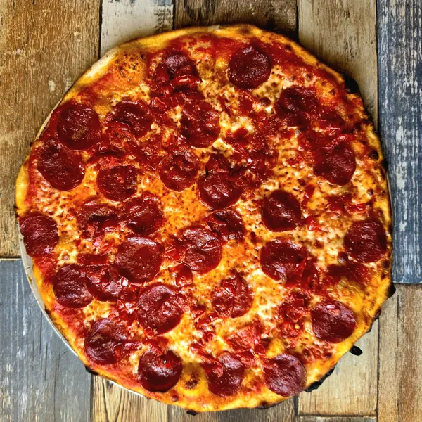 A round pizza covered edge to edge with pepperoni and chopped tomato