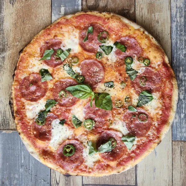 A red pizza with salami, sliced jalapeños, fresh basil and black pepper