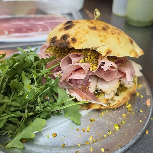 A sandwich of cured meats, chicken and crushed pistachio on a charred roll, with arugula