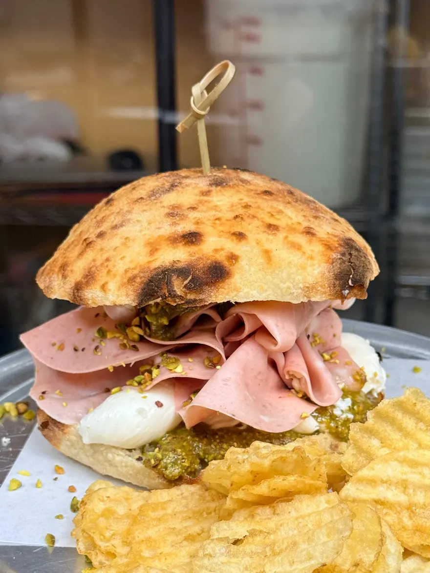 The Full Monti sandwich: shaved mortadella, smashed burrata and pistachio pesto on a charred sourdough puccia, with crinkle-cut chips