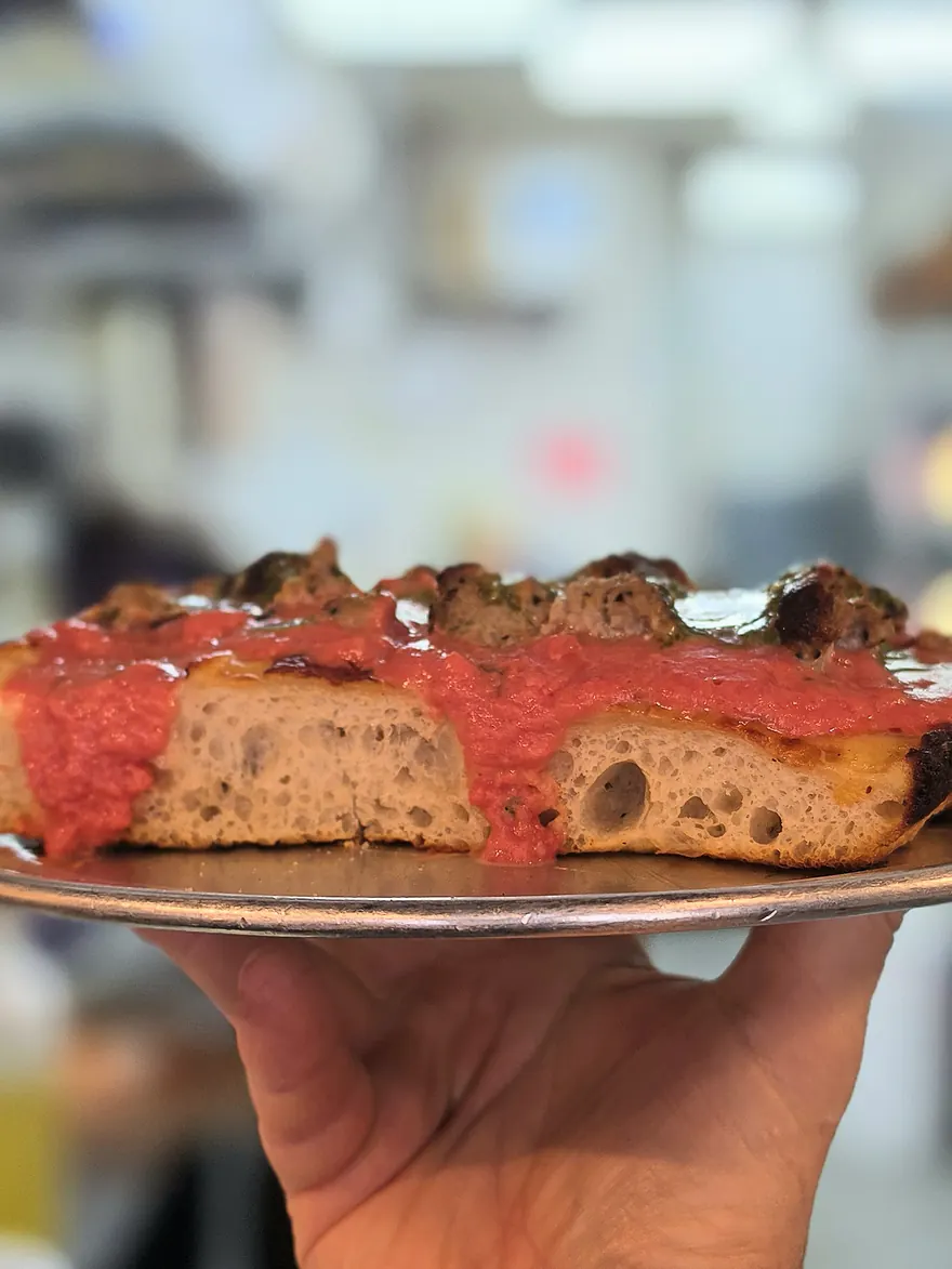 The Meatball Square: a thick, airy sourdough focaccia slice with beef meatballs, vodka sauce and pesto, held up on a tray